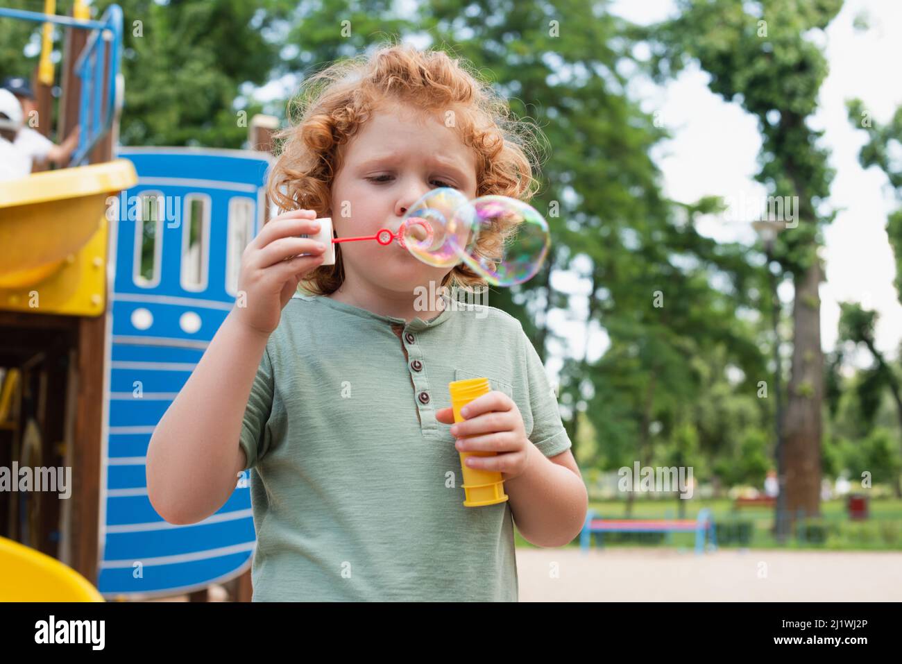 curly kid blowing soap bubbles on playground Stock Photo
