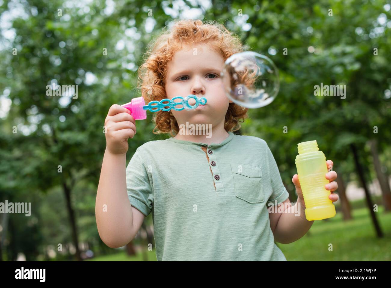 redhead boy blowing soap bubble in summer park Stock Photo