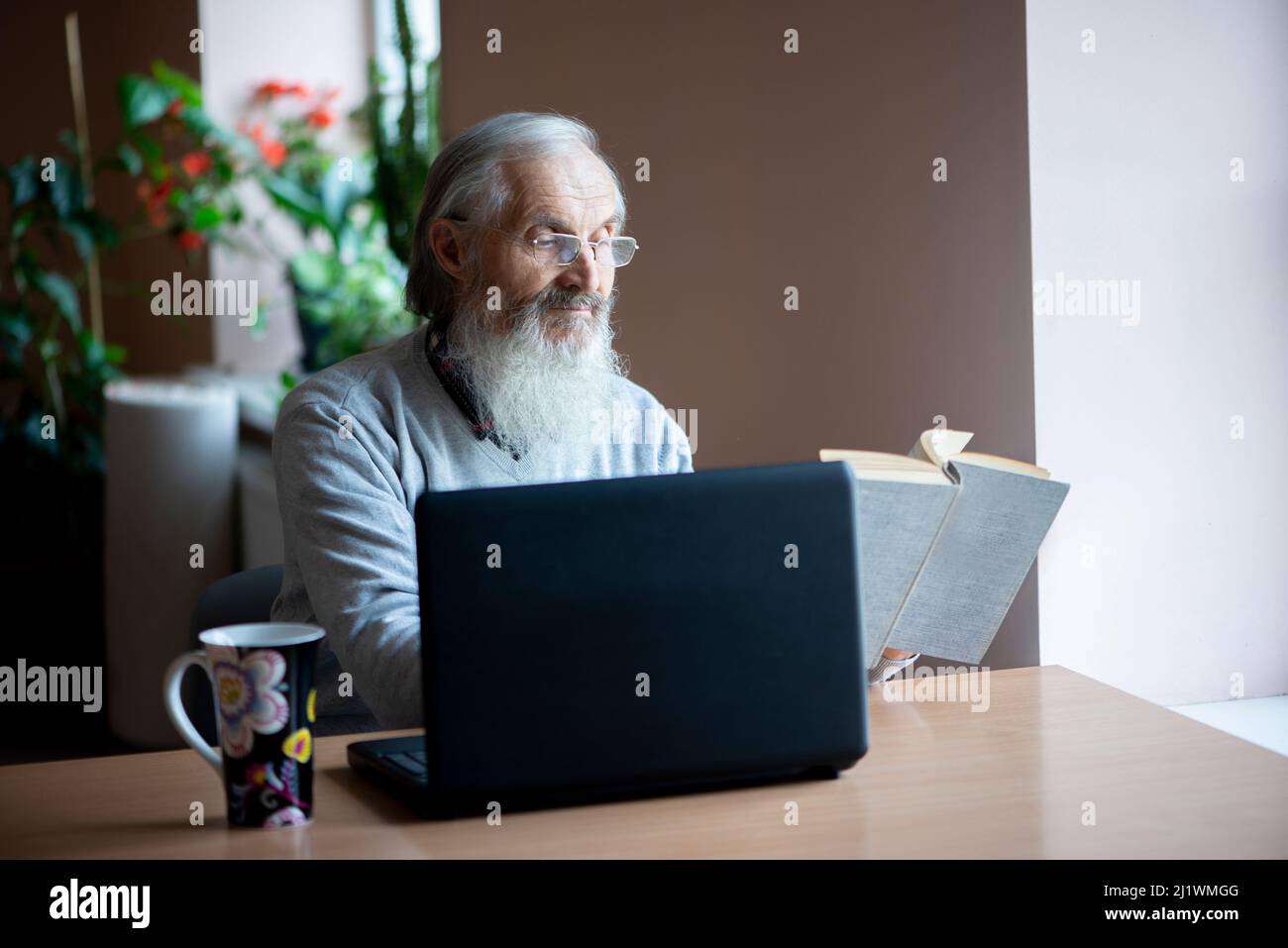 senior man reading book and using laptop computer Stock Photo
