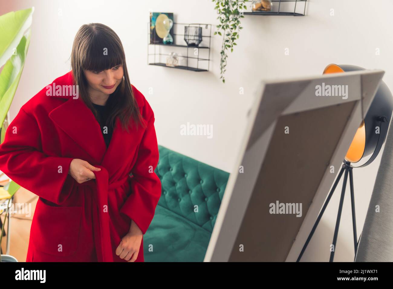 Caucasian brown-haired woman trying out warm red coat in front of mirror. Online shopping concept. High quality photo Stock Photo