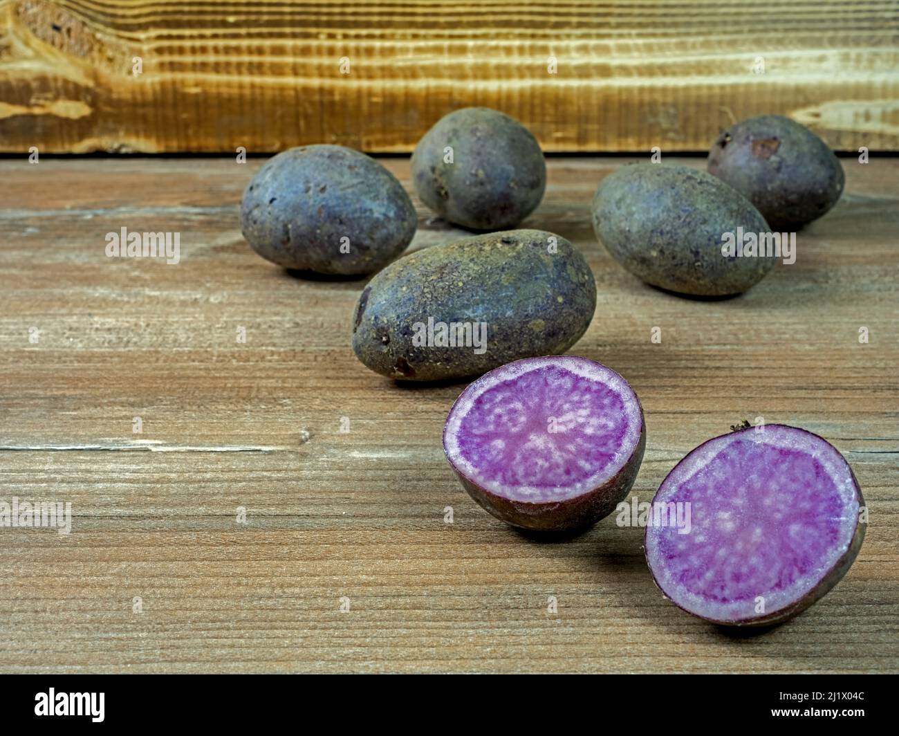 Several potatoes of purple variety Violetta on wood in front of a wooden box, one potato cut Stock Photo