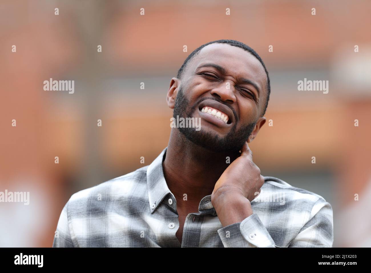 Front view portrait of a man with black skin with neck ache complaining in the street Stock Photo