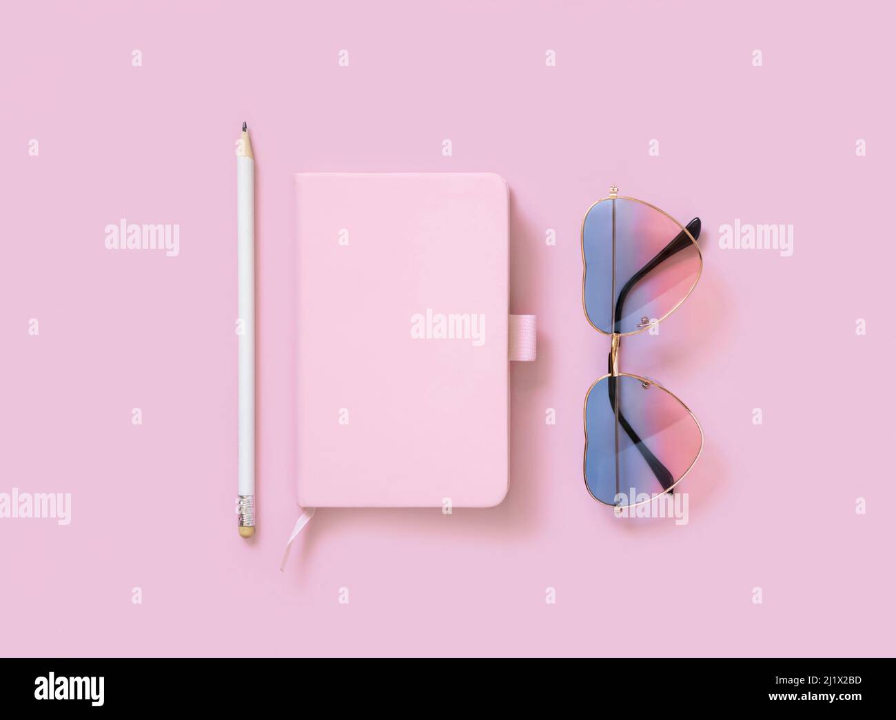 Hardcover textbook, heart sunglases and pensil on pink. Hardcover notebook mockup flat lay.  Femminine girly and Travel concept Stock Photo