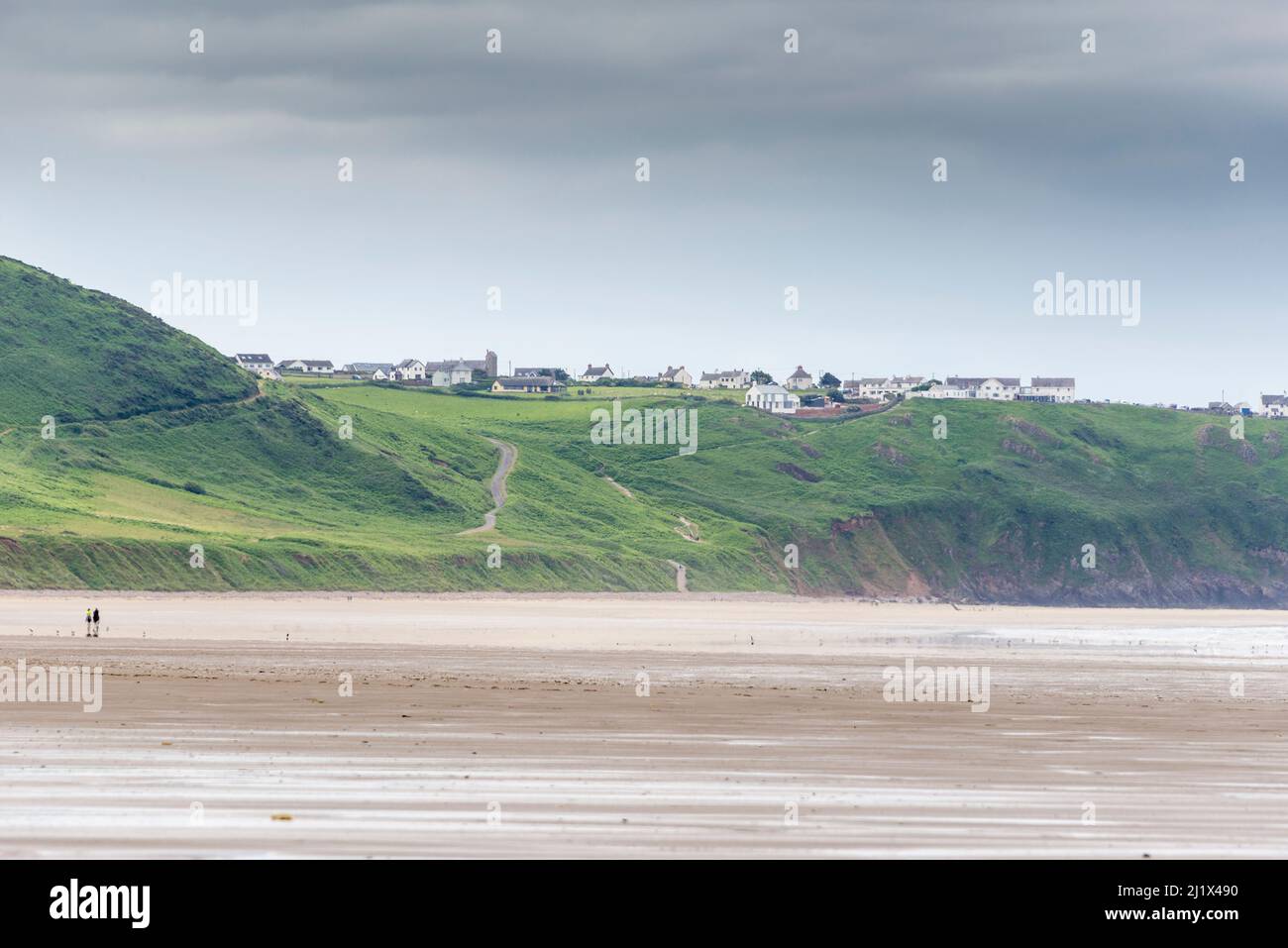 An expansive view along the huge sandy beach at Rhossili Bay at low tide.  In the distance is Rhossili Down and the the clifftop village of Rhossili. Stock Photo