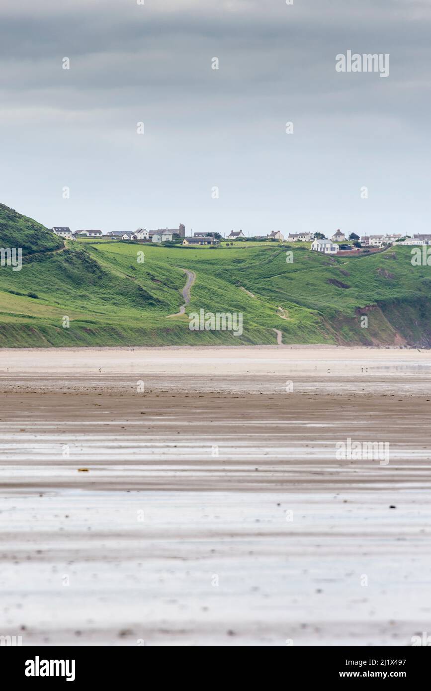 An expansive view along the huge sandy beach at Rhossili Bay at low tide.  In the distance is Rhossili Down and the the clifftop village of Rhossili. Stock Photo