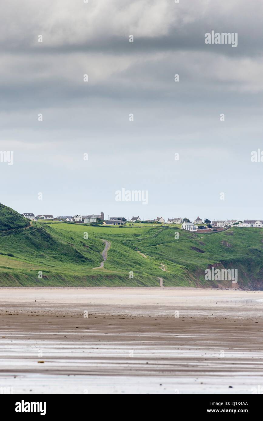 A view along the huge sandy beach at Rhossili Bay at low tide.  In the distance is Rhossili Down and the the clifftop village of Rhossili. Stock Photo