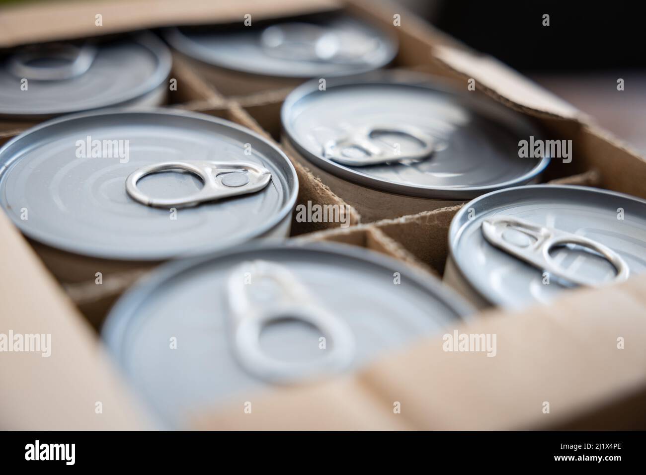 Food cans in an open cardboard box. Concept image for supply chain disruption, food shortage, stockpiling in times of war. Selective focus. Stock Photo
