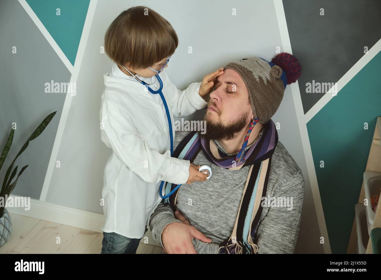 Father and child playing clinic and doctor, little boy in medical gown with stethoscope treats dad Stock Photo
