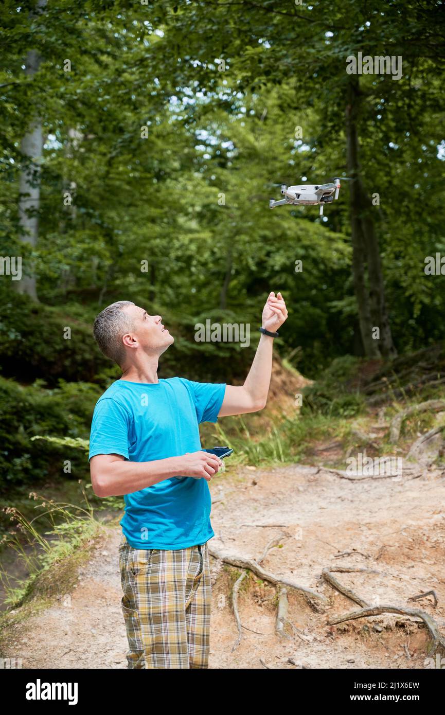 Man operating drone using remote controller. Man using drone for photos and video making while standing in green forest. Stock Photo