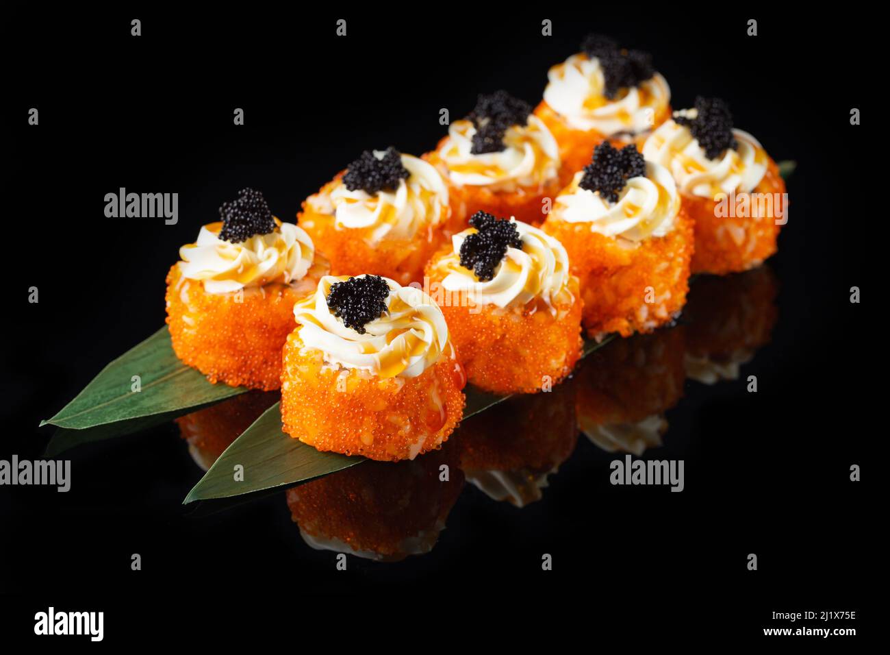 Traditional delicious fresh sushi roll set on a black background with reflection. Sushi roll with rice, nori, cream cheese, tobiko caviar, avocado. Su Stock Photo