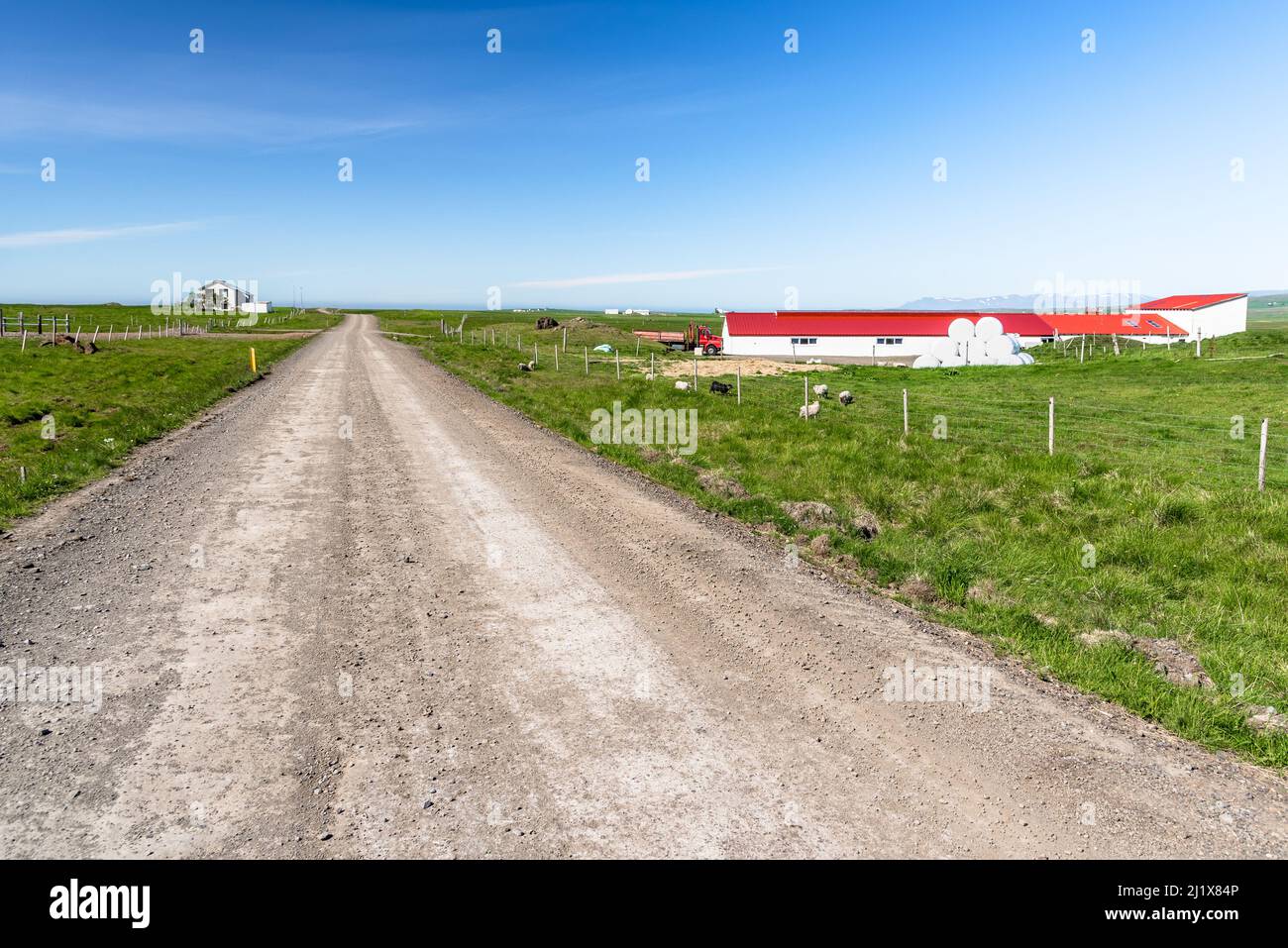Farm buildings along a straight gravel road in the countryside on a clear summer day Stock Photo