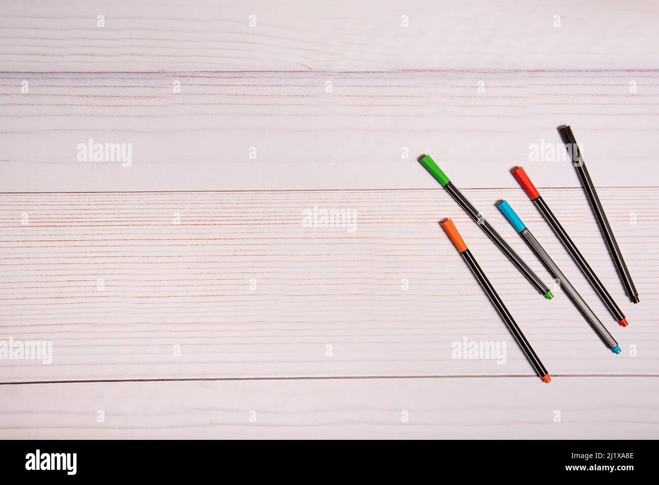 PENS OF DIFFERENT COLORS, ON WHITE WOODEN TABLE. Stock Photo