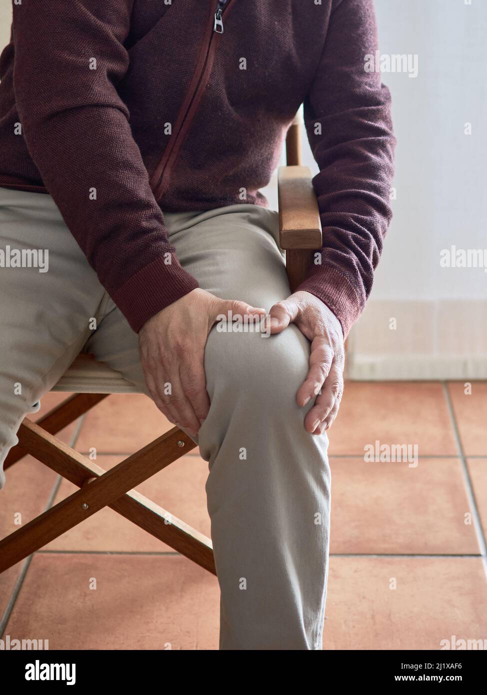 A vertical shot of a male clutching his knee in pain from osteoarthritis Stock Photo
