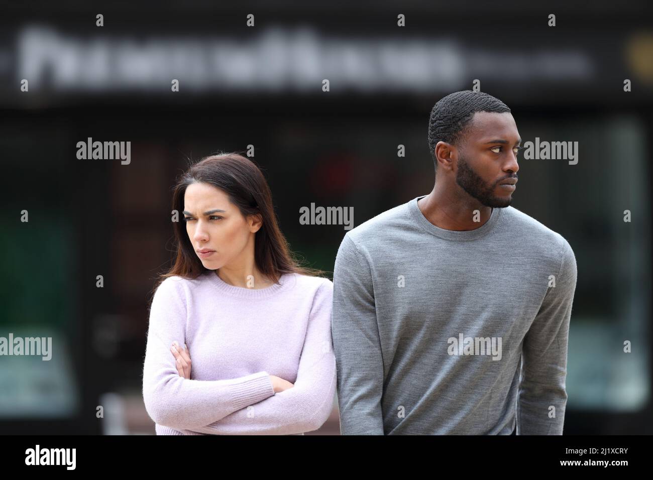 Front view portrait of an angry interracial couple ignoring each other walking in the street Stock Photo
