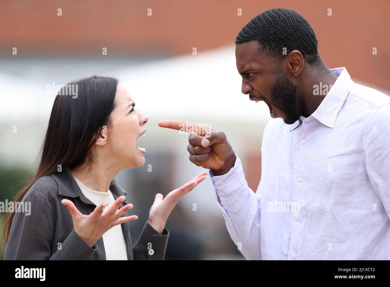 Angry man arguing and pointing to a woman in the street Stock Photo