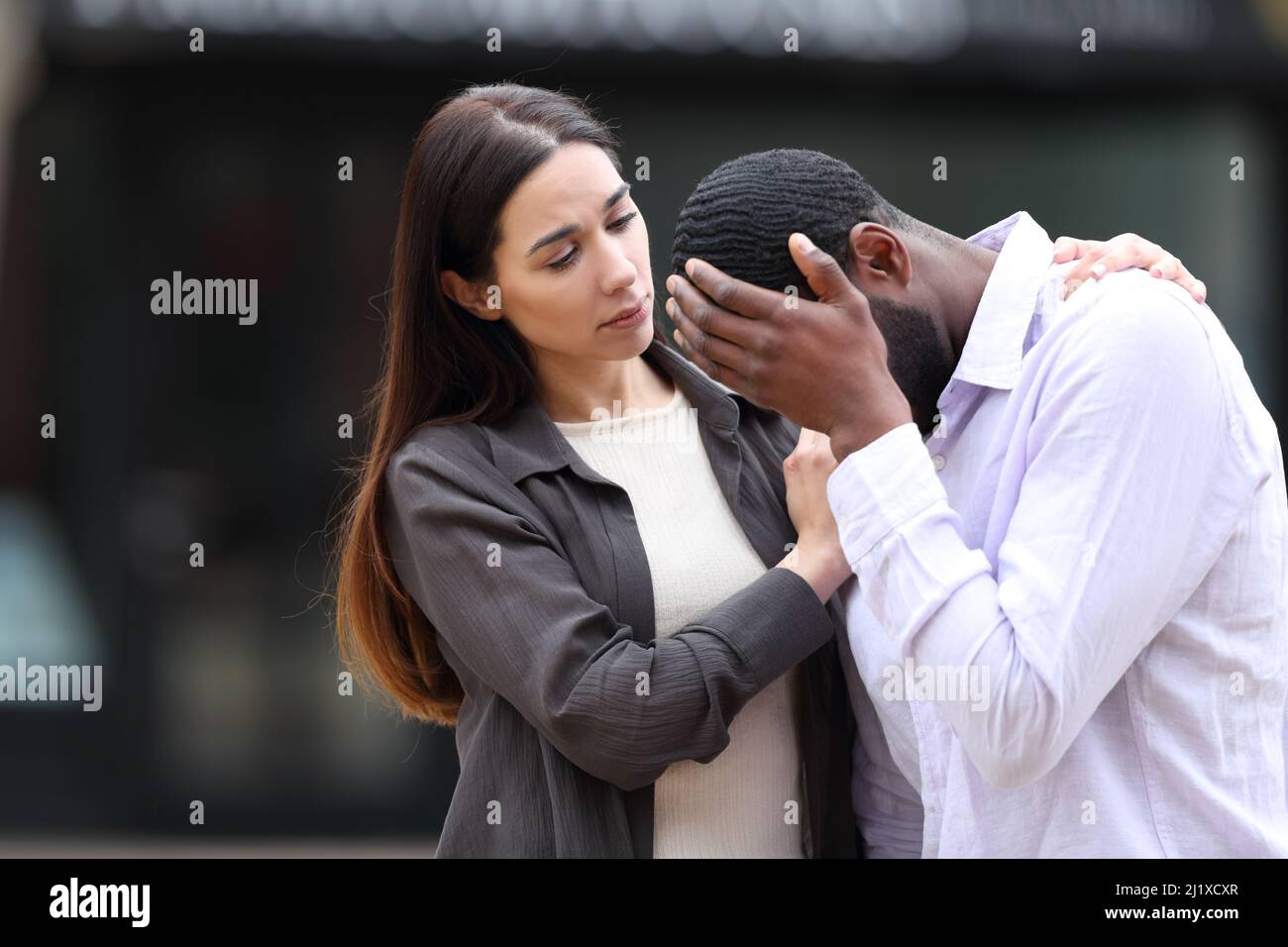 Worried woman comforting a sad friend in the street Stock Photo