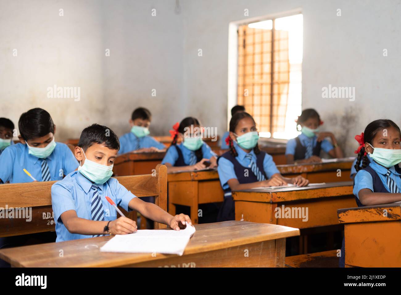 Focus on behind kids, pan shot of school children with medical face mask and social distance listening class at school - concept of protection from Stock Photo