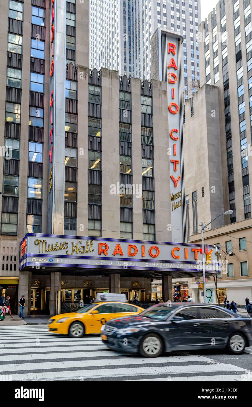 Radio City Music Hall New York City with crosswalk and traffic, a yellow  taxi and black car in the forefront during daytime, vertical Stock Photo -  Alamy