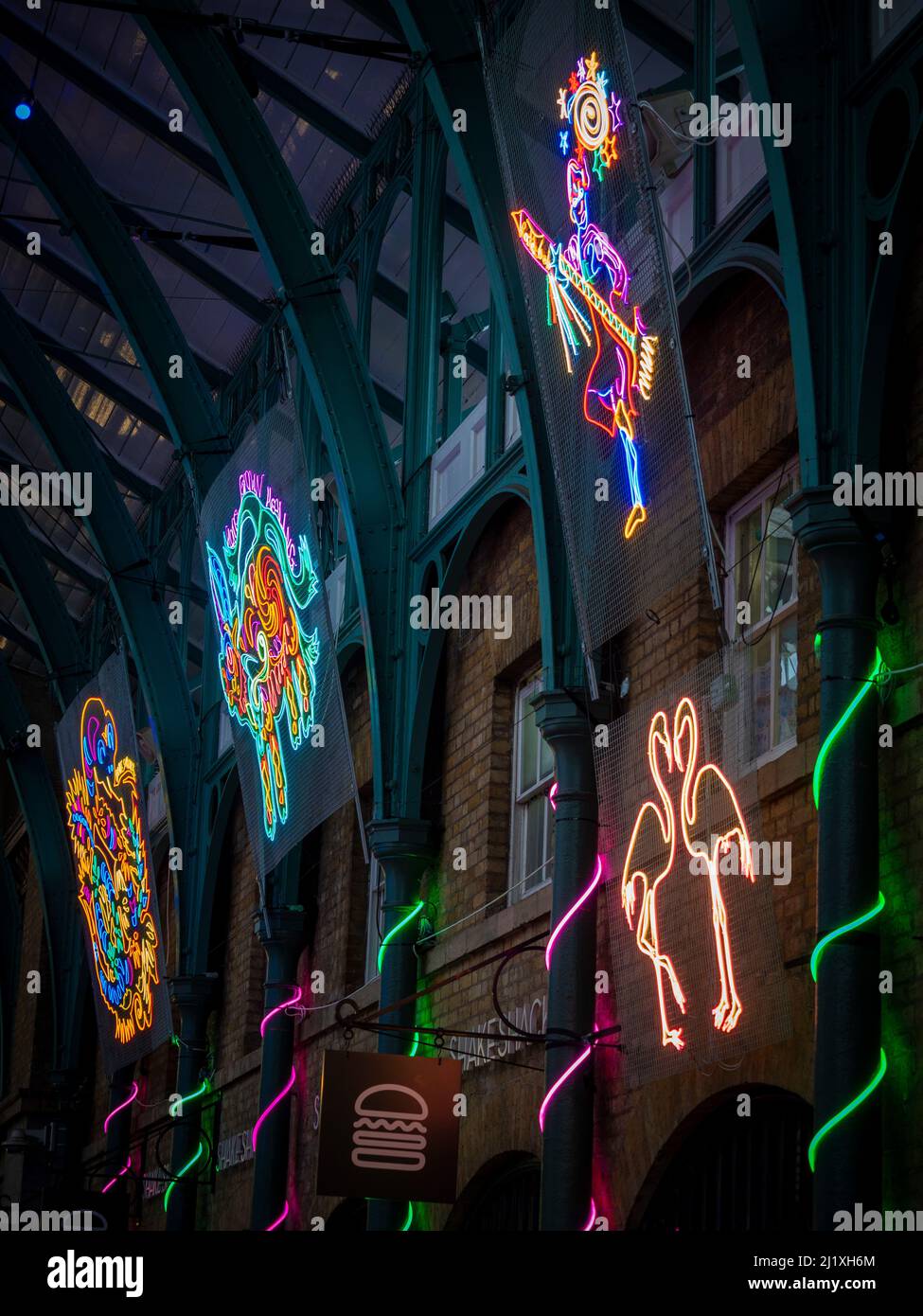 2D neon light art installations by Chila Burman suspended between metal roof trusses of the Market Hall at Covent Garden, London. Stock Photo