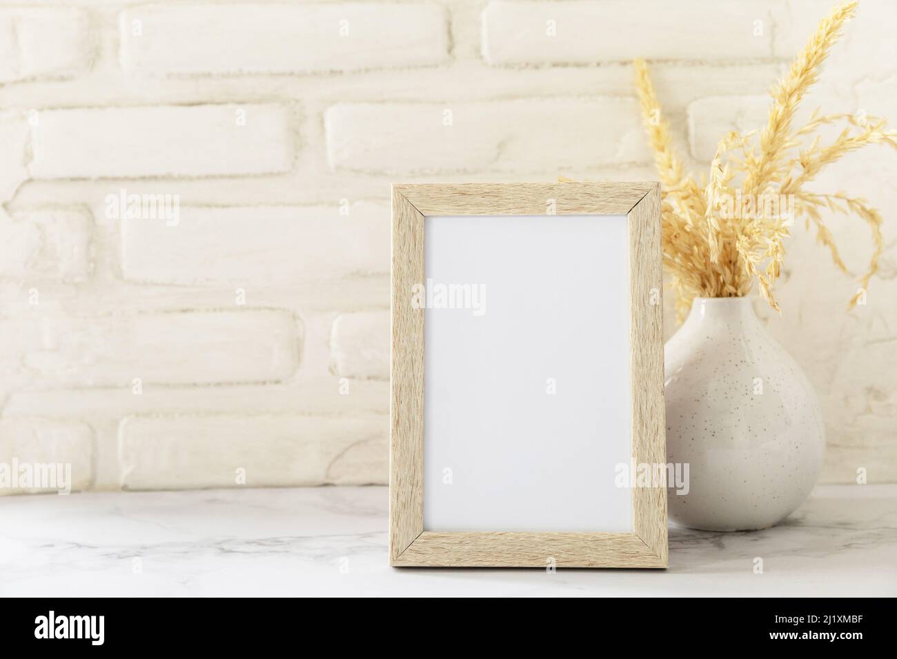 White picture frame mockup. White wall background. Scandinavian interior, neutral color palette with dry grass. Selective focus. Stock Photo
