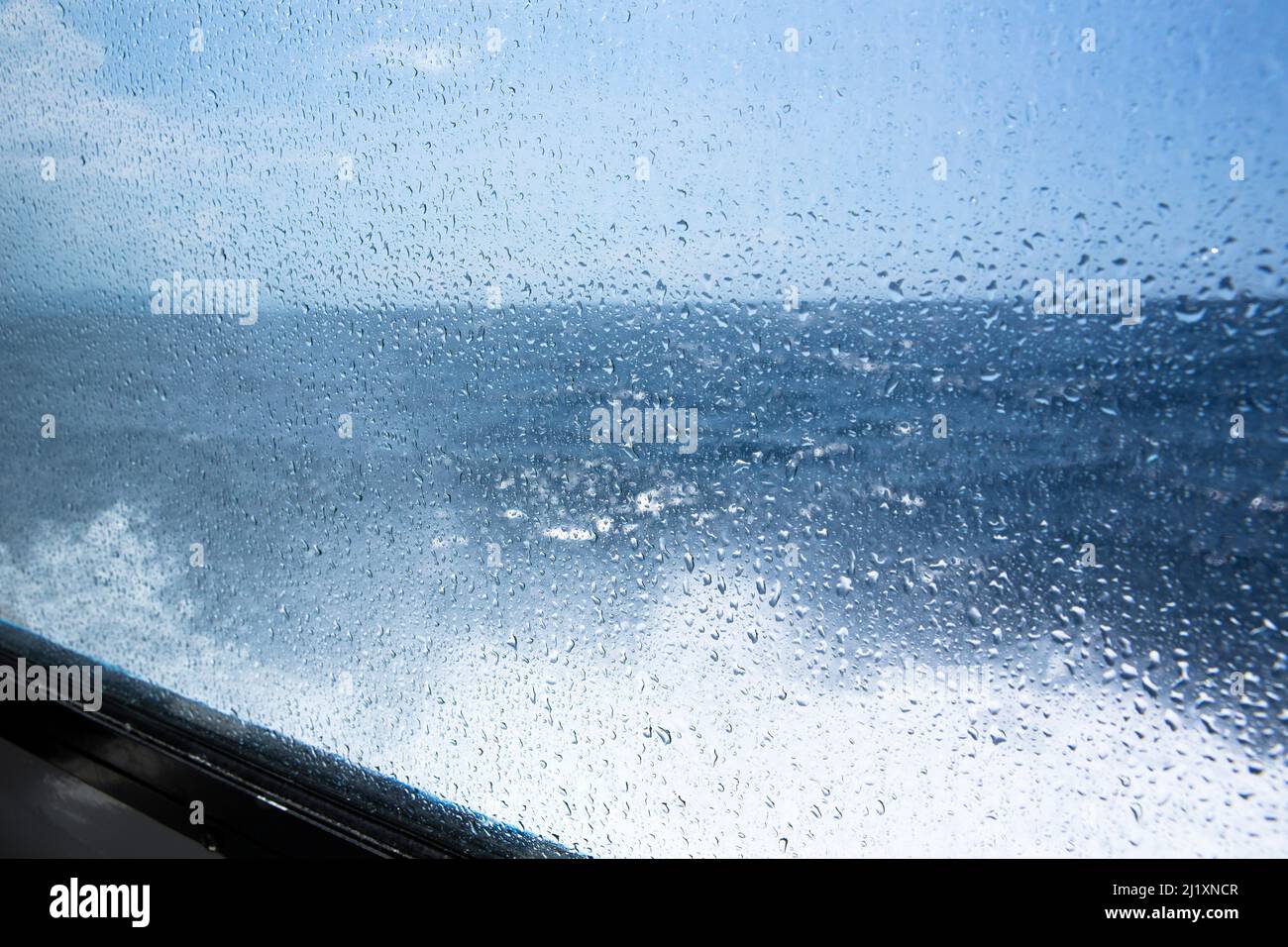 Looking out of the window of a tourist boat at the sea, weather trhough water drops on the glass on the northern Italian coastline. Stock Photo