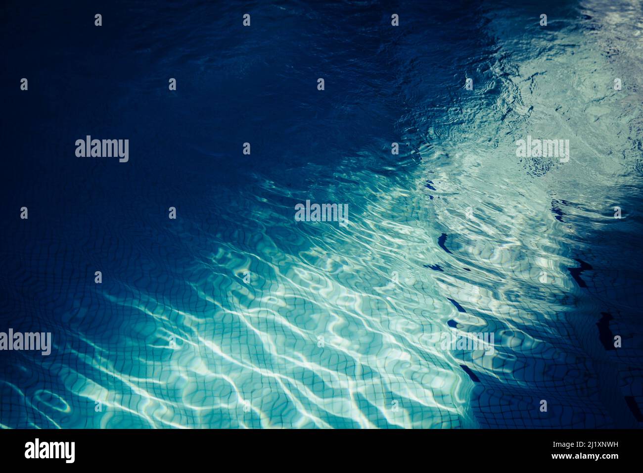 A swimming pool with clear blue water, ripples on the surafce and a ...