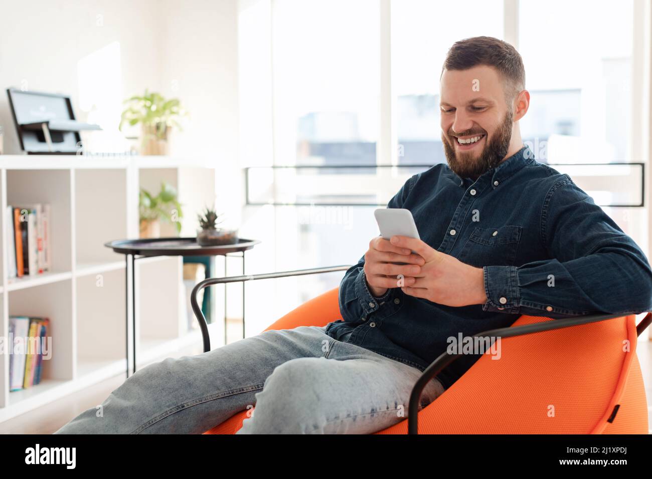 Cheerful Bearded Man Using Mobile Phone Texting Sitting At Home Stock Photo