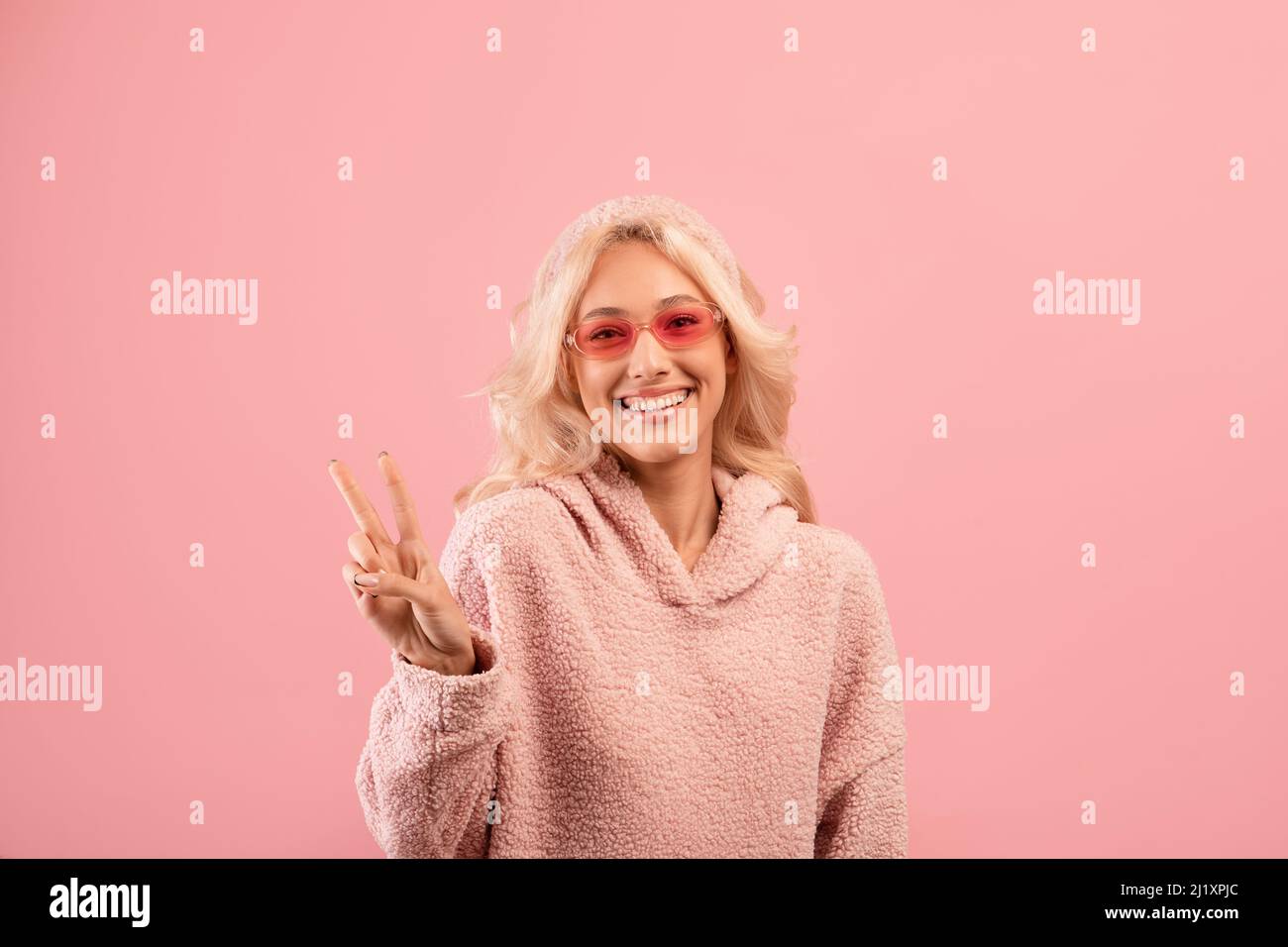 Good mood. Happy stylish lady showing victory v sign and smiling at camera, wearing colorful sunglasses Stock Photo