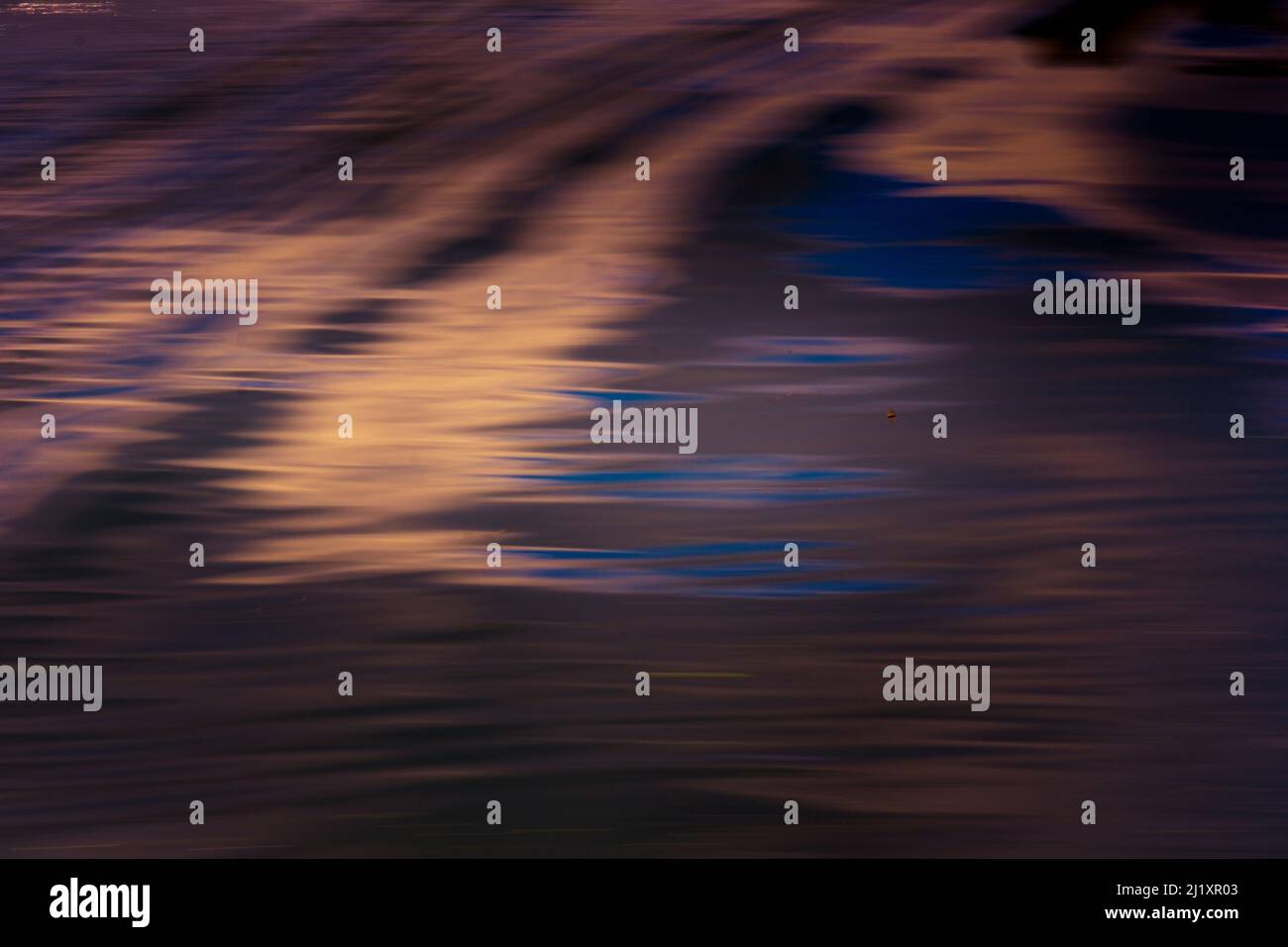 Small waves and ripples reflecting the colourful sky on the surface of ...