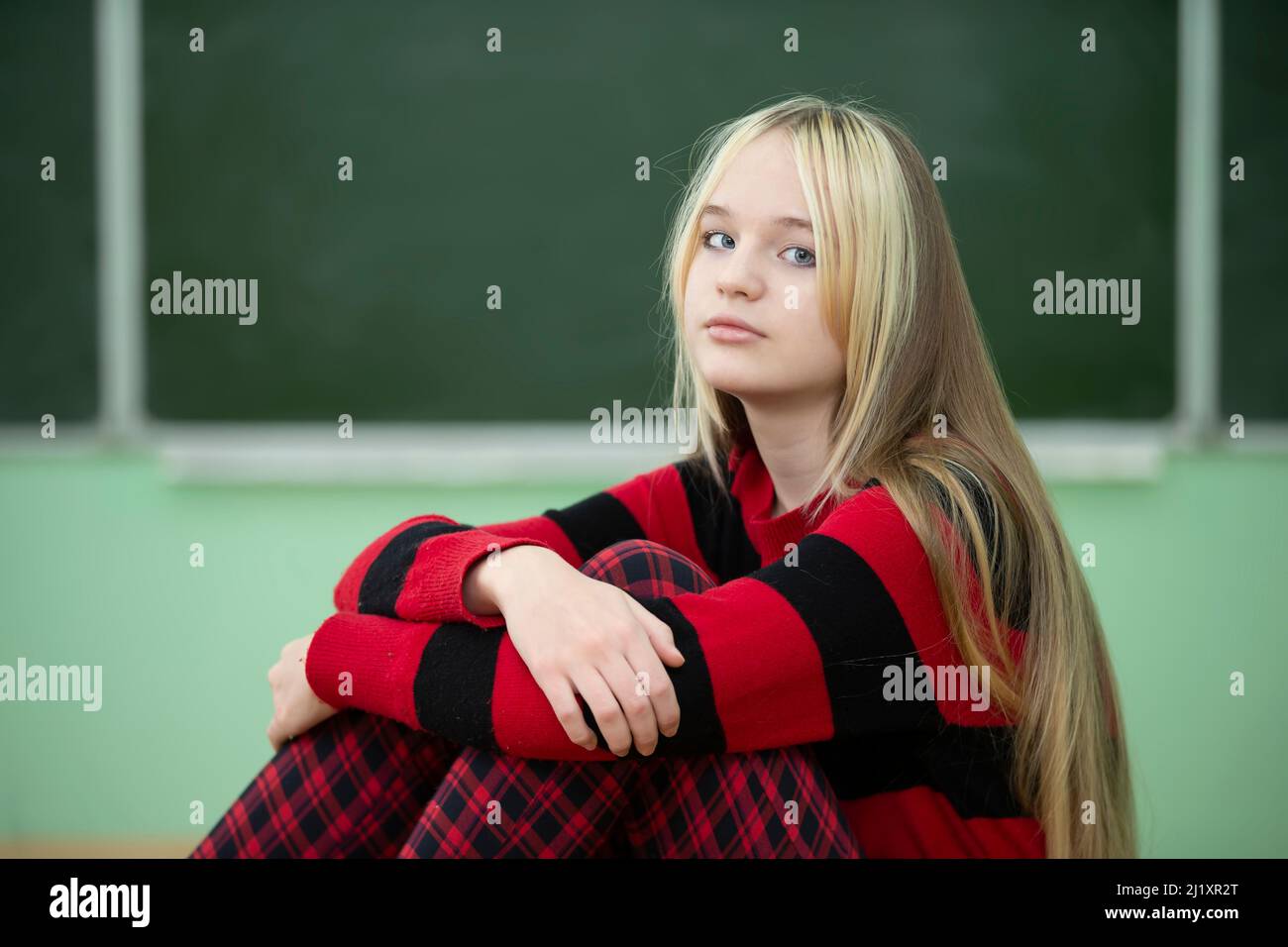 Teenager of senior school age. A teenage girl sits on the background of a blackboard and looks at the camera. Stock Photo