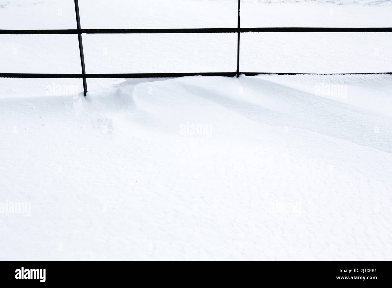 A metal fence partially buried under mounds of drifting snow. Stock Photo