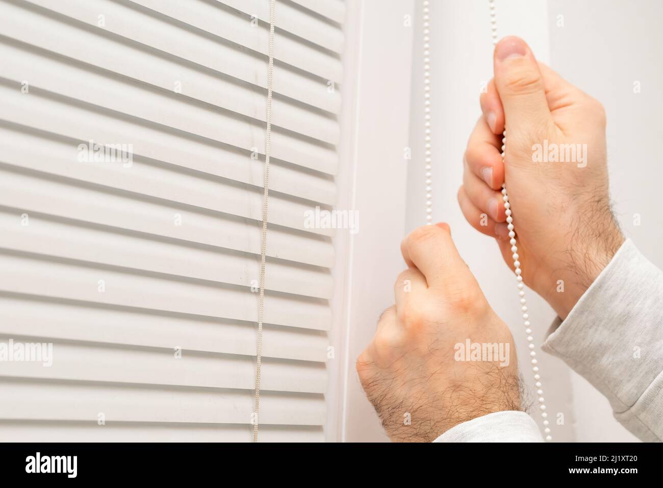 Close up man hand opening horizontal window blinds with copy space