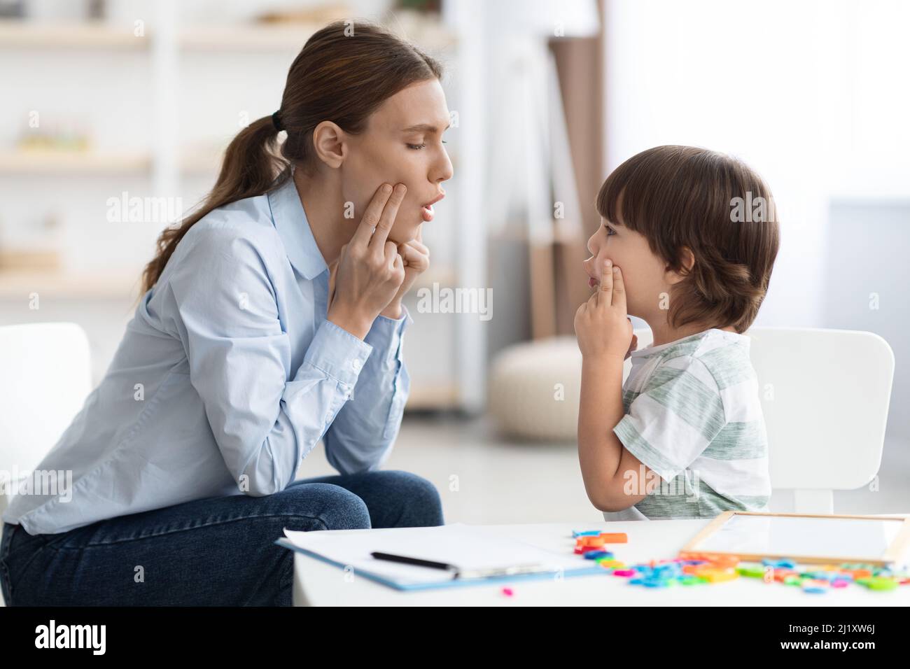 Cute little boy training with professional speech specialist, repeating