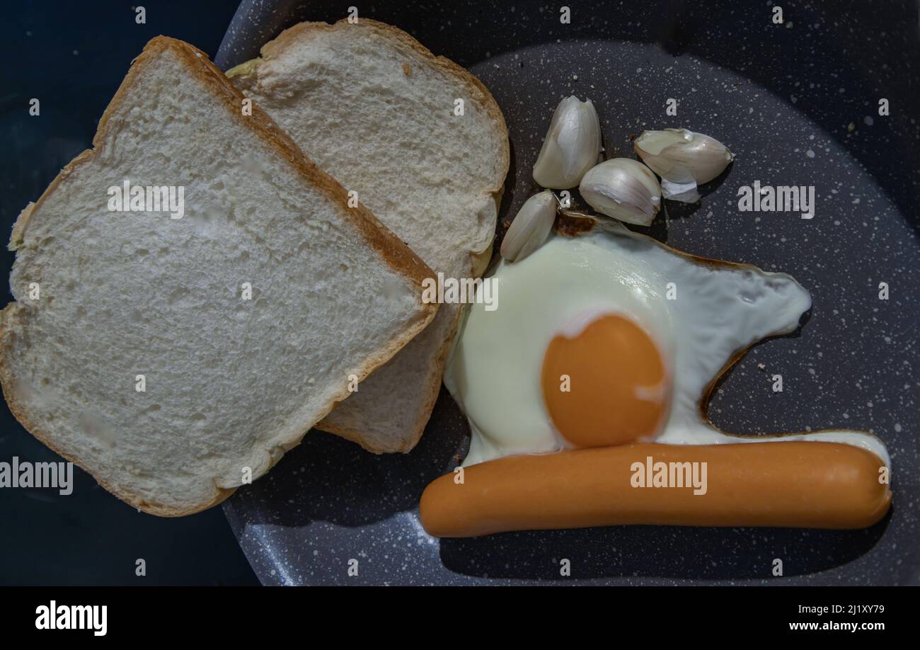 Preparing Breakfast in Cooking pan with Fried egg, Fried sausages Garlic and Two breads. Space for text, Selective focuse. Stock Photo