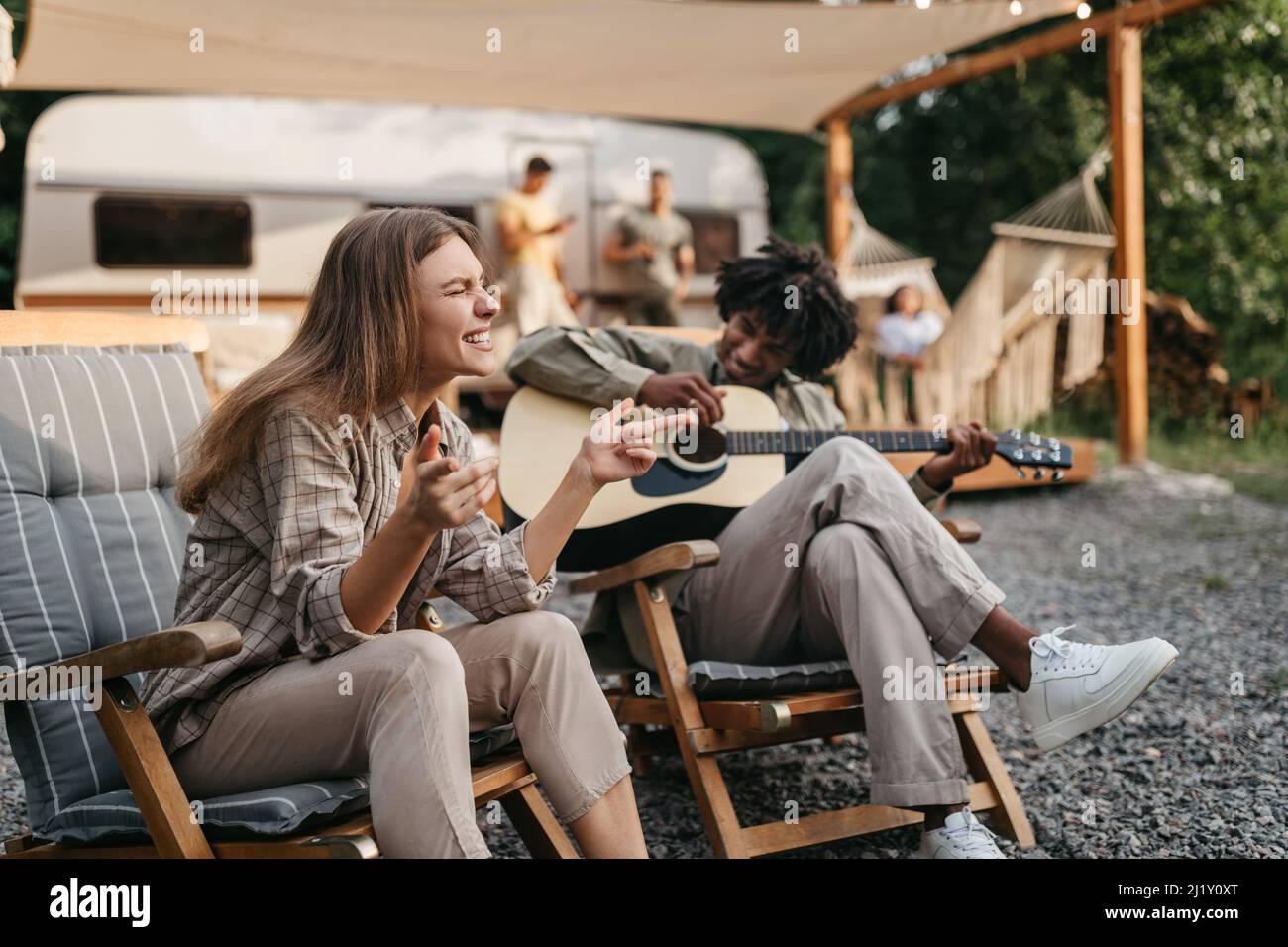 Happy black guy playing guitar, his female friend singing, sitting in