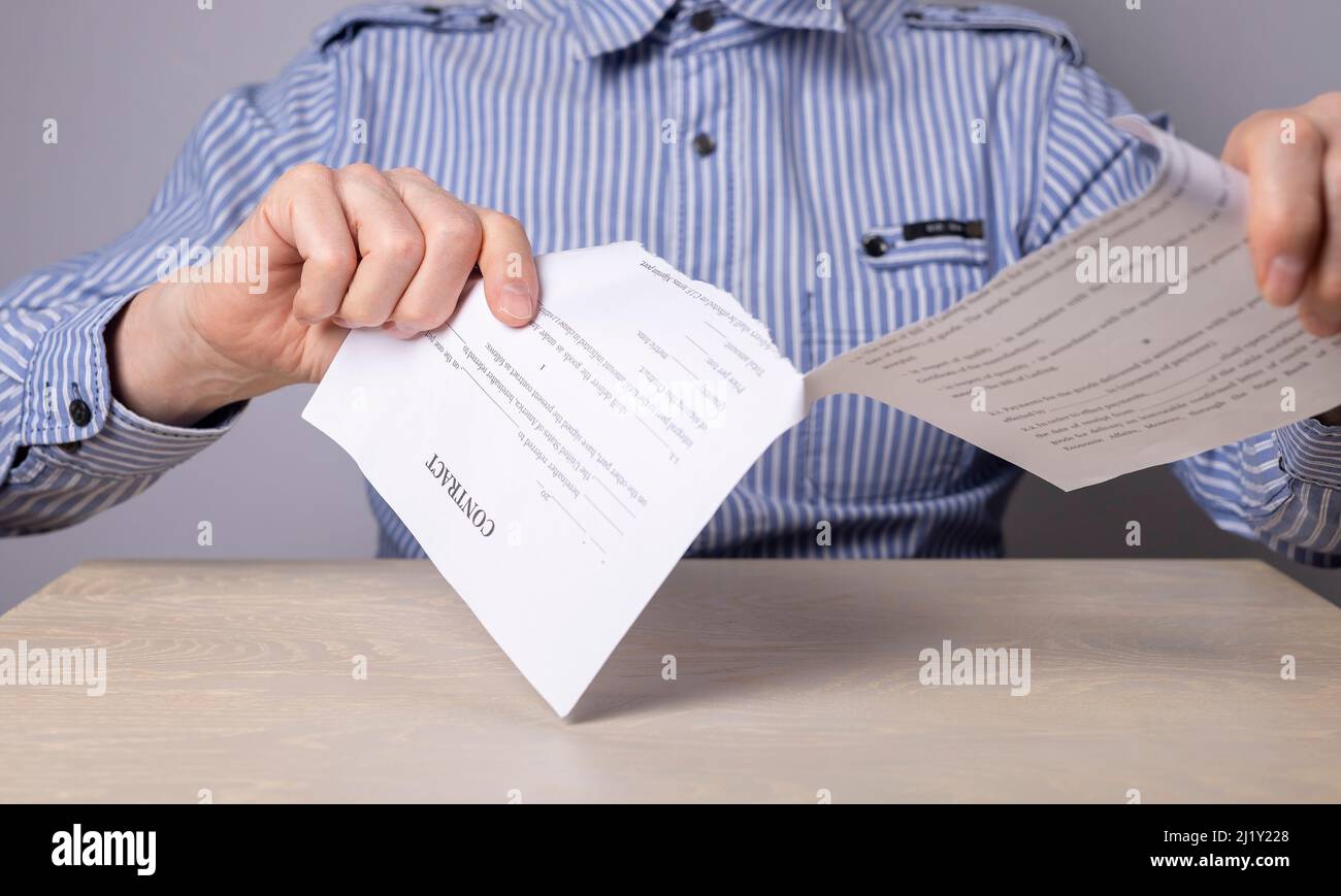 Man hands closeup tearing contract. Cancellation of deal or arrangement. Dismissal concept. Man sitting at table in office and breaking document. High quality photo Stock Photo