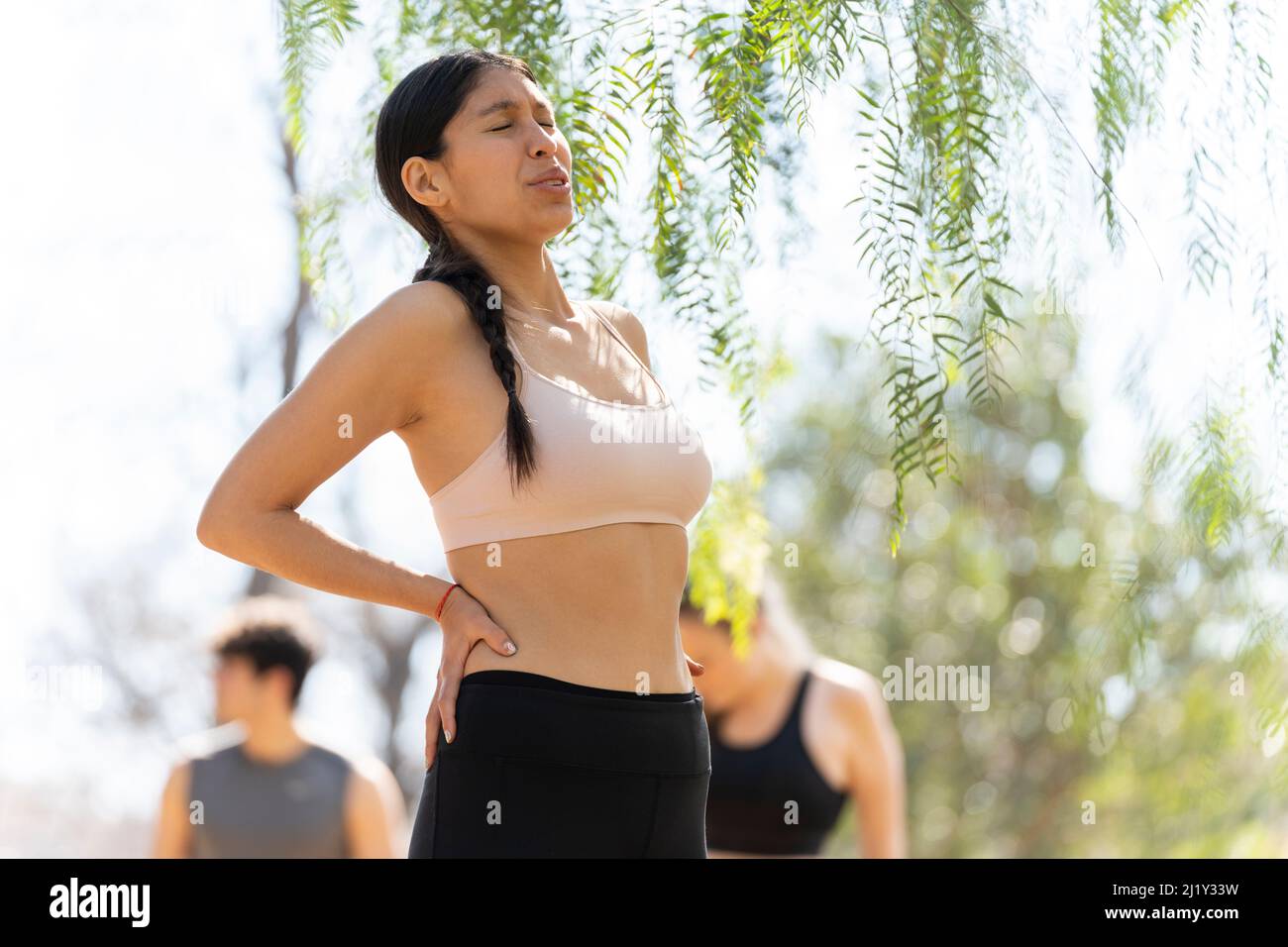 Hispanic young woman expresses back pain while doing sports Stock Photo