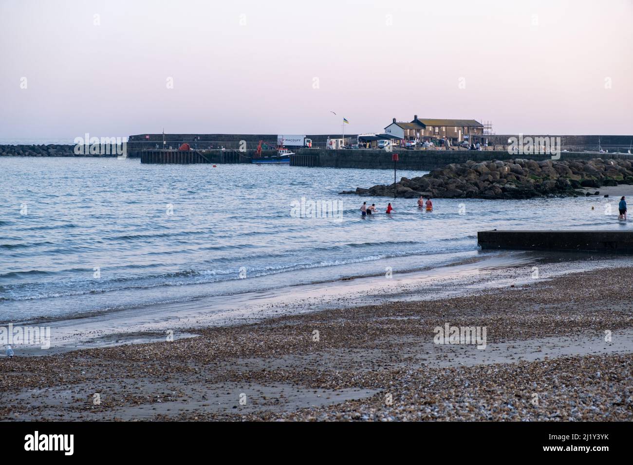 Teenagers playing in the sae at dusk in Lyme Regis, UK (Mar22) Stock Photo