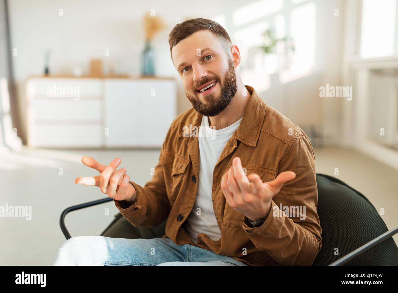 Cheerful Bearded Millennial Man Talking Sitting In Chair At Home Stock Photo