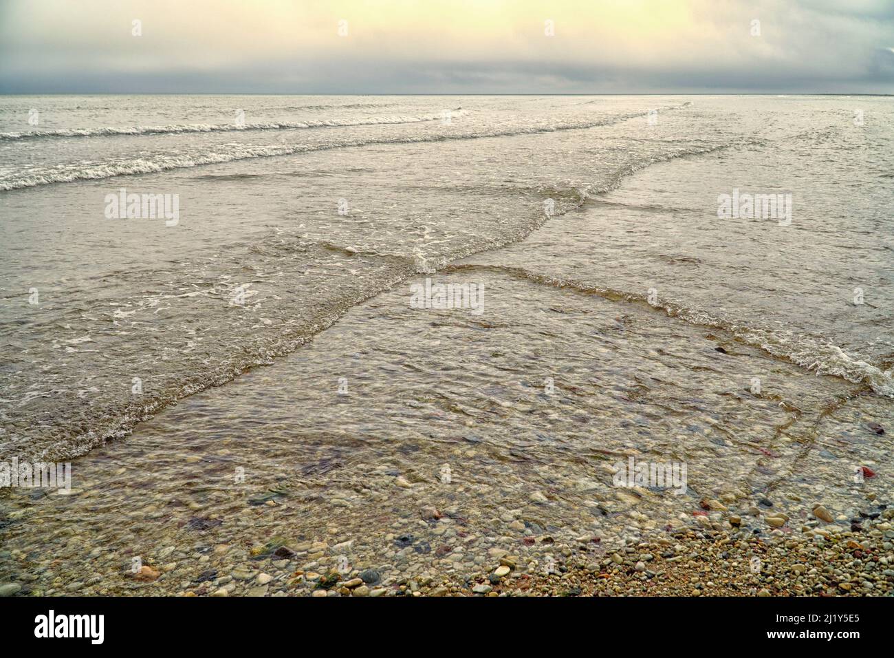 Overlapping, intersecting waves on seashore with dramatic cloudy sky  illuminated by the sun. Natural background, pattern, texture of water. Interfere Stock Photo