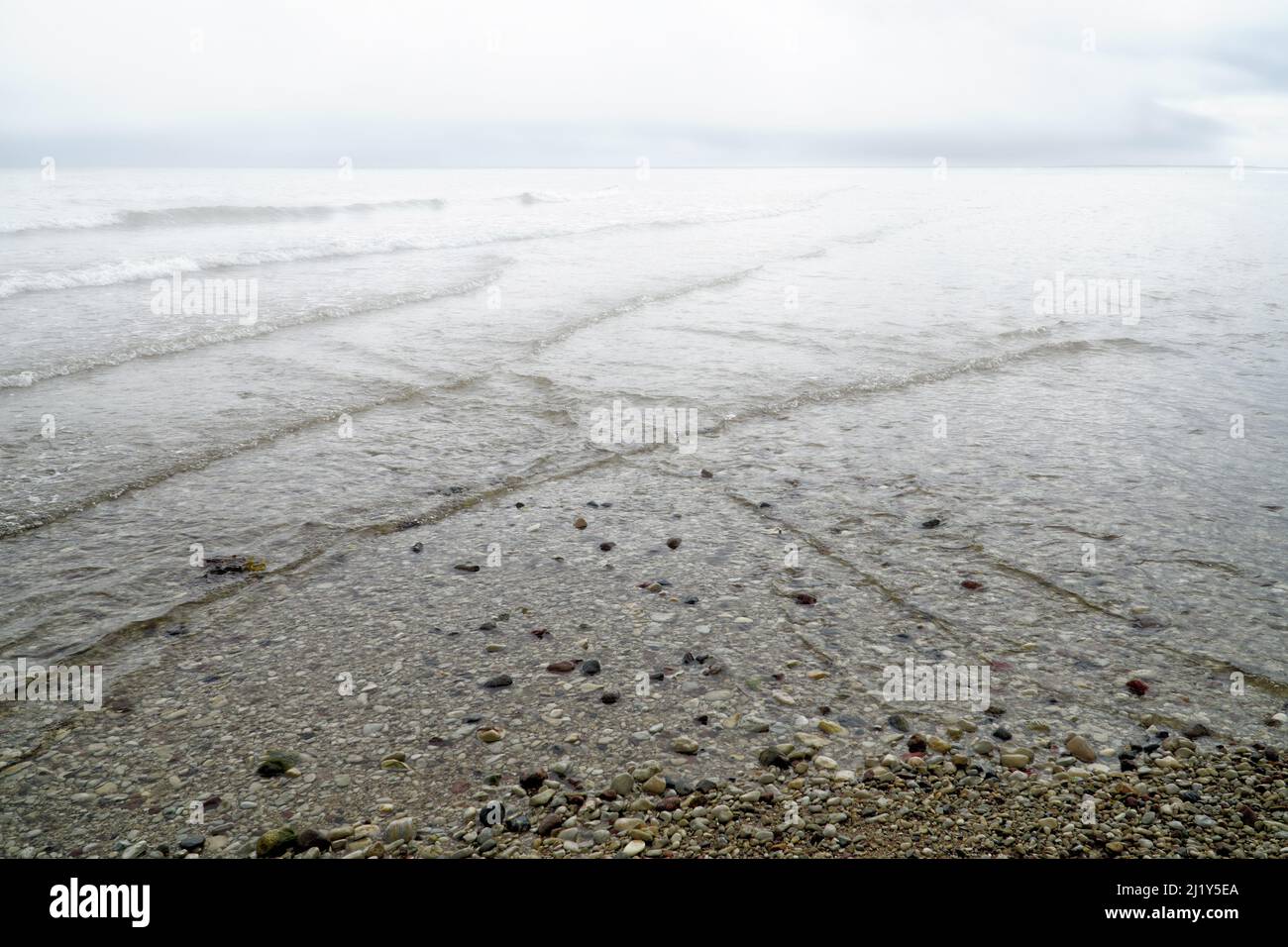 Overlapping, intersecting waves on seashore covered with fog with dramatic cloudy sky. Natural hazy background, pattern, texture of water. Interferenc Stock Photo