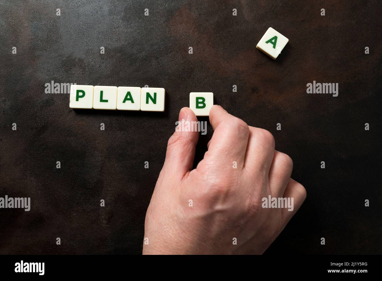 Detail of a hand forming the phrase PLAN B with pieces of letters, the letter A appears apart. Concept of second chance, resilience and constancy. Dar Stock Photo