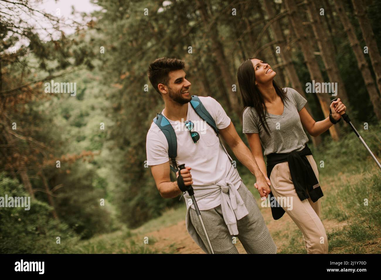 Couple of young hikers with backpacks walk through the forest Stock Photo