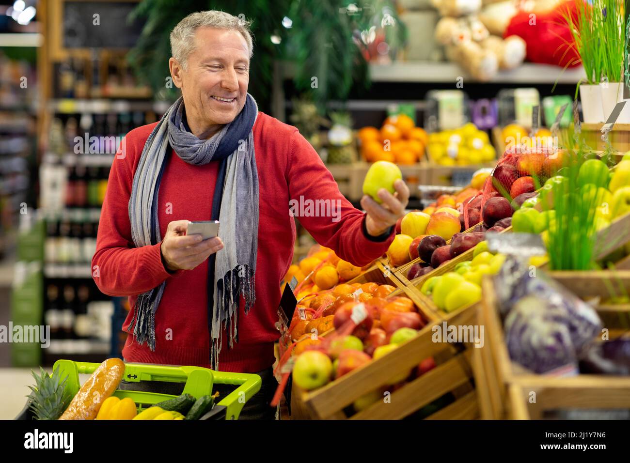 Smiling man using cell phone while shopping at supermarket Stock Photo