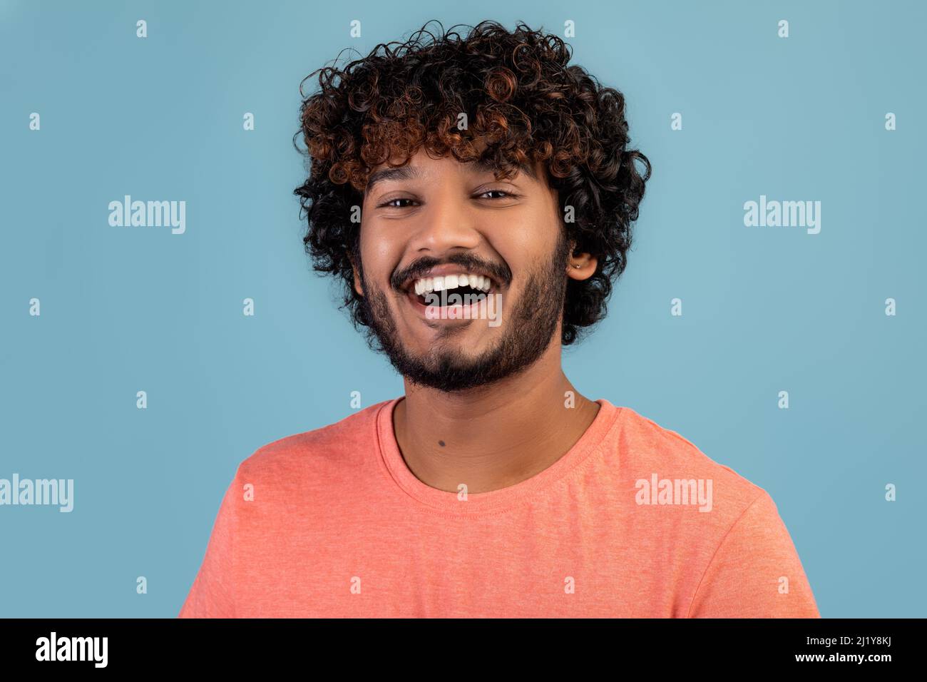 Portrait of cheerful handsome indian young man on blue Stock Photo