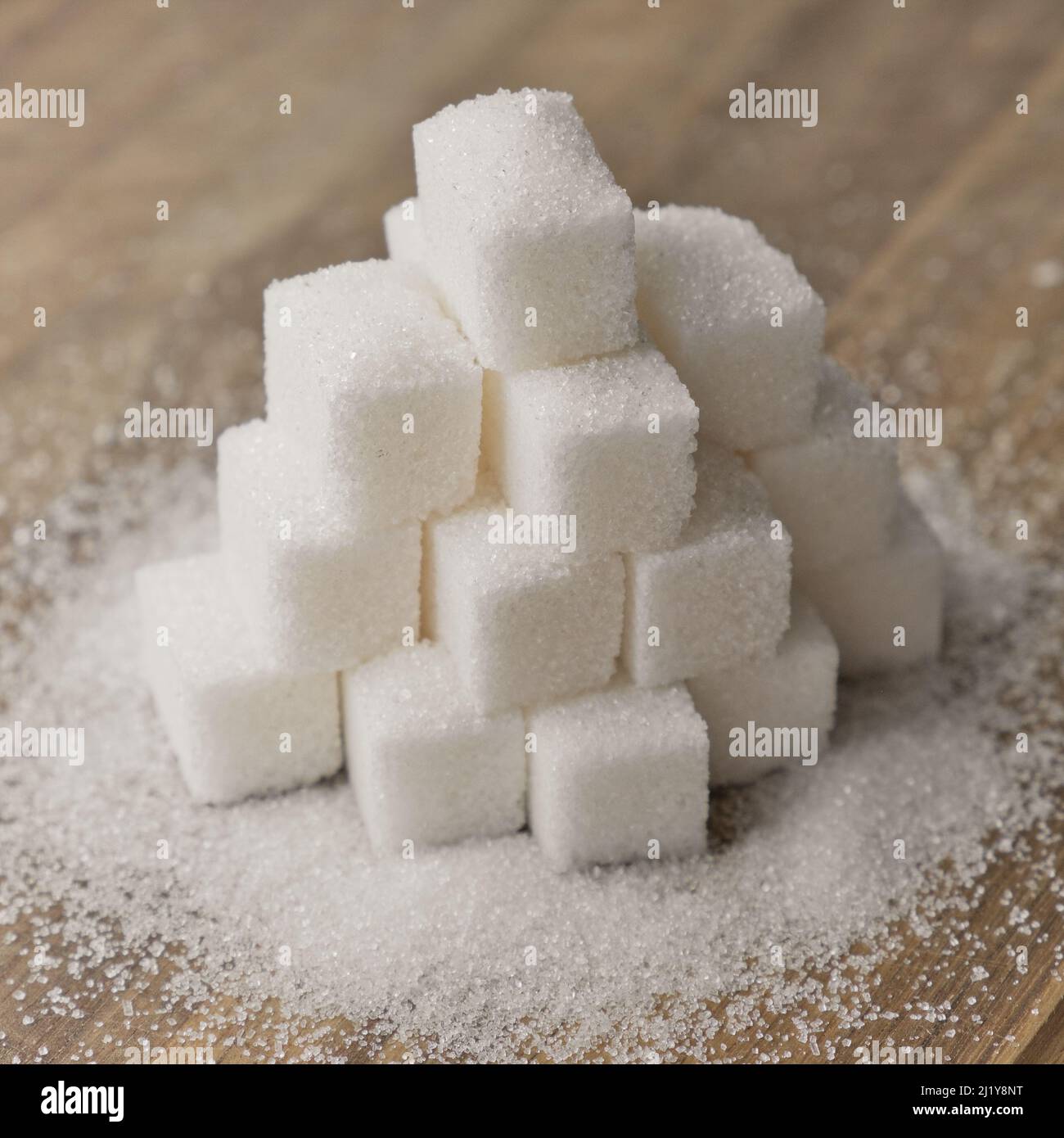 Lump sugar stacked in pyramid on wooden table. Sugar scattered on ...