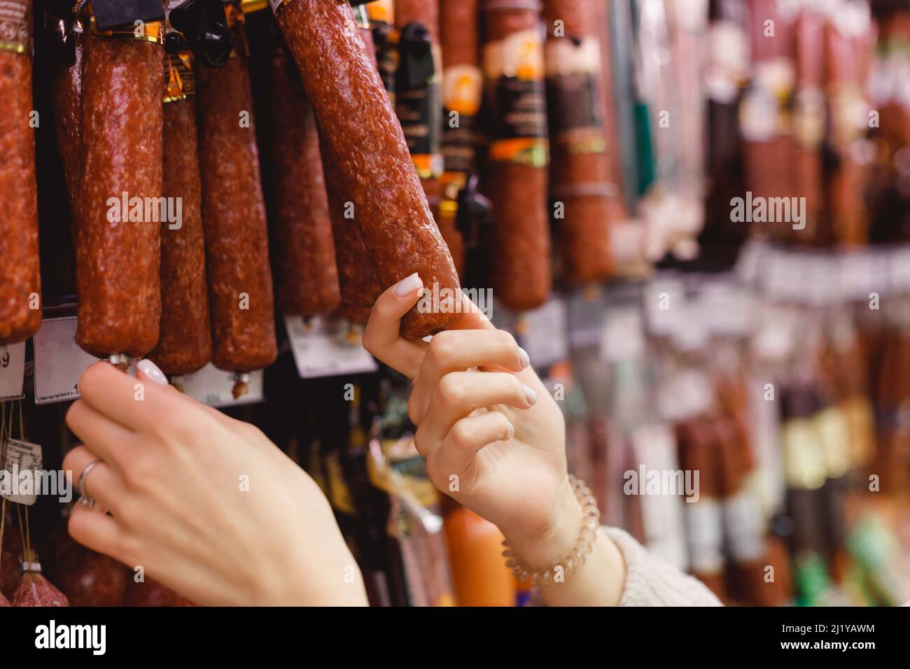 Woman chooses dried smoked sausage hanging in refrigerator in butcher's shop Stock Photo Alamy