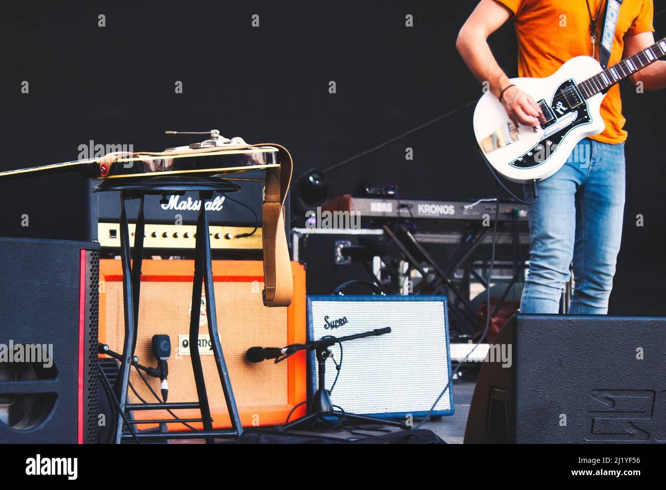 A guitarist on stage surrounded by musical equipment and electric guitar amplifiers Stock Photo