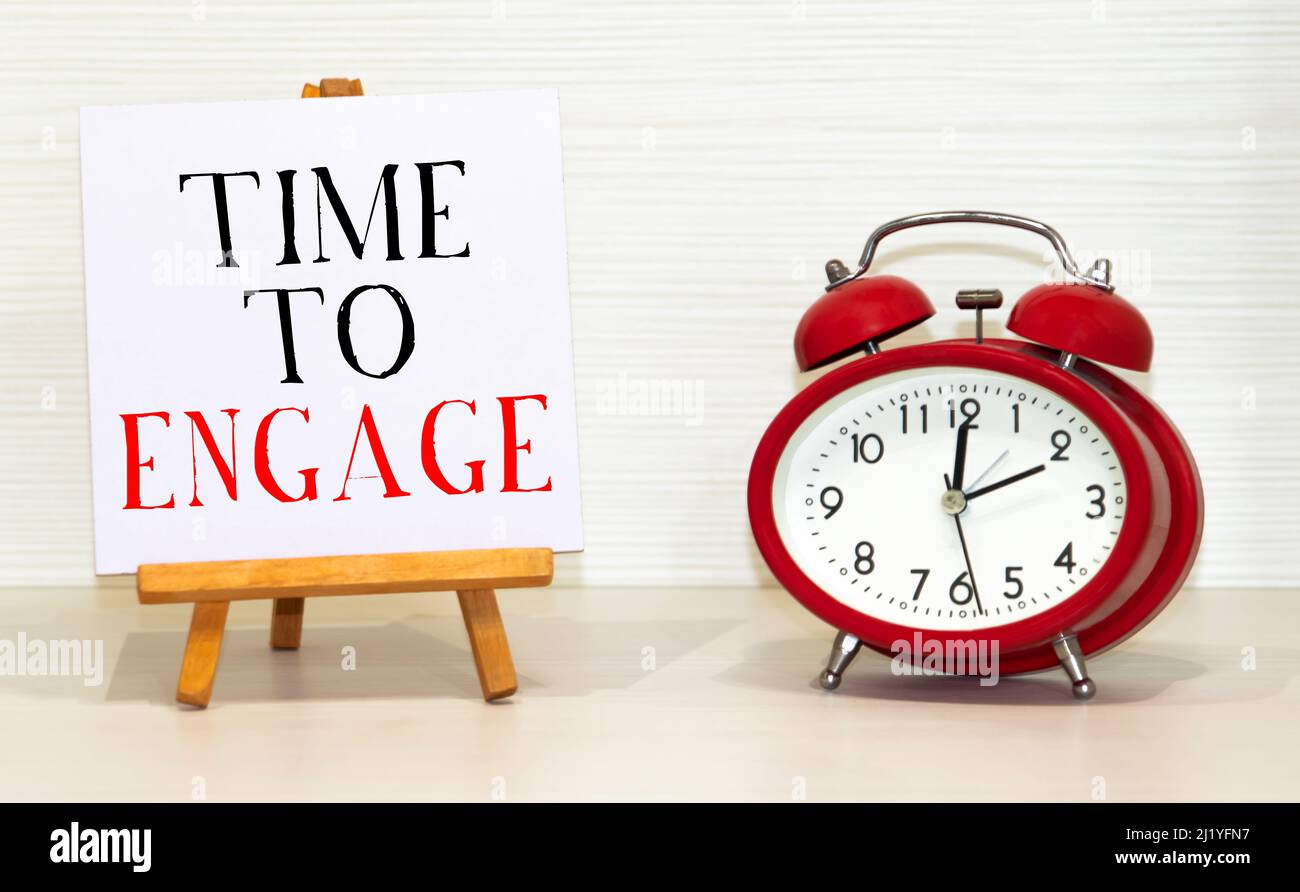 Alarm clock and note with phrase TIME TO ENGAGE on white background