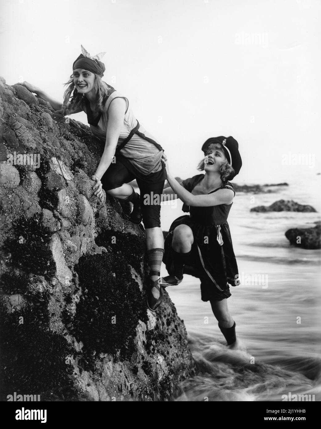 Two women in 1920's attire on the beach climbing on the rocks at the beach Stock Photo